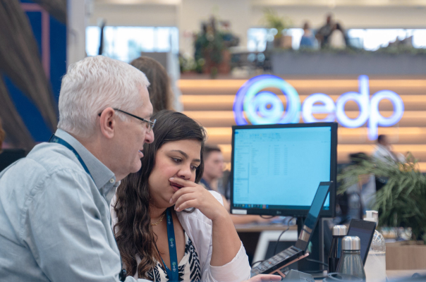 white haired man side by side with a younger woman, wearing long dark hair, both looking at a laptop screen