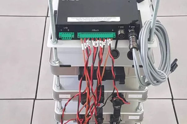 stack of connected battery modules with a battery management system (bms) on top, featuring labeled connectors and wires for monitoring and controlling energy storage