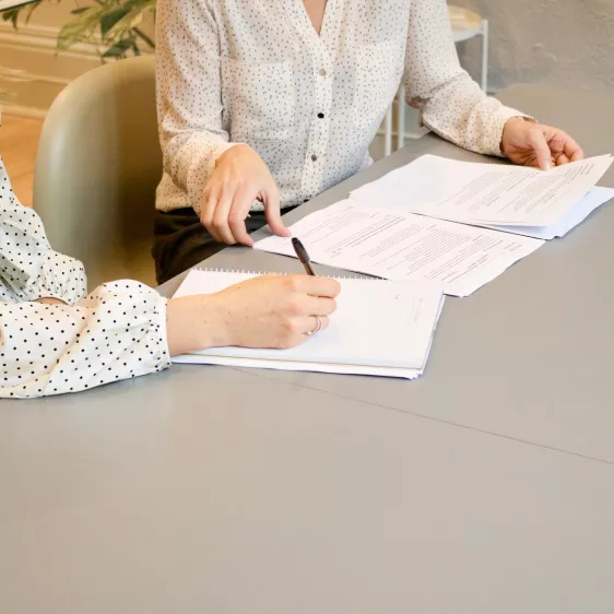 duas mulheres sentadas a uma secretária com papéis e canetas na mão