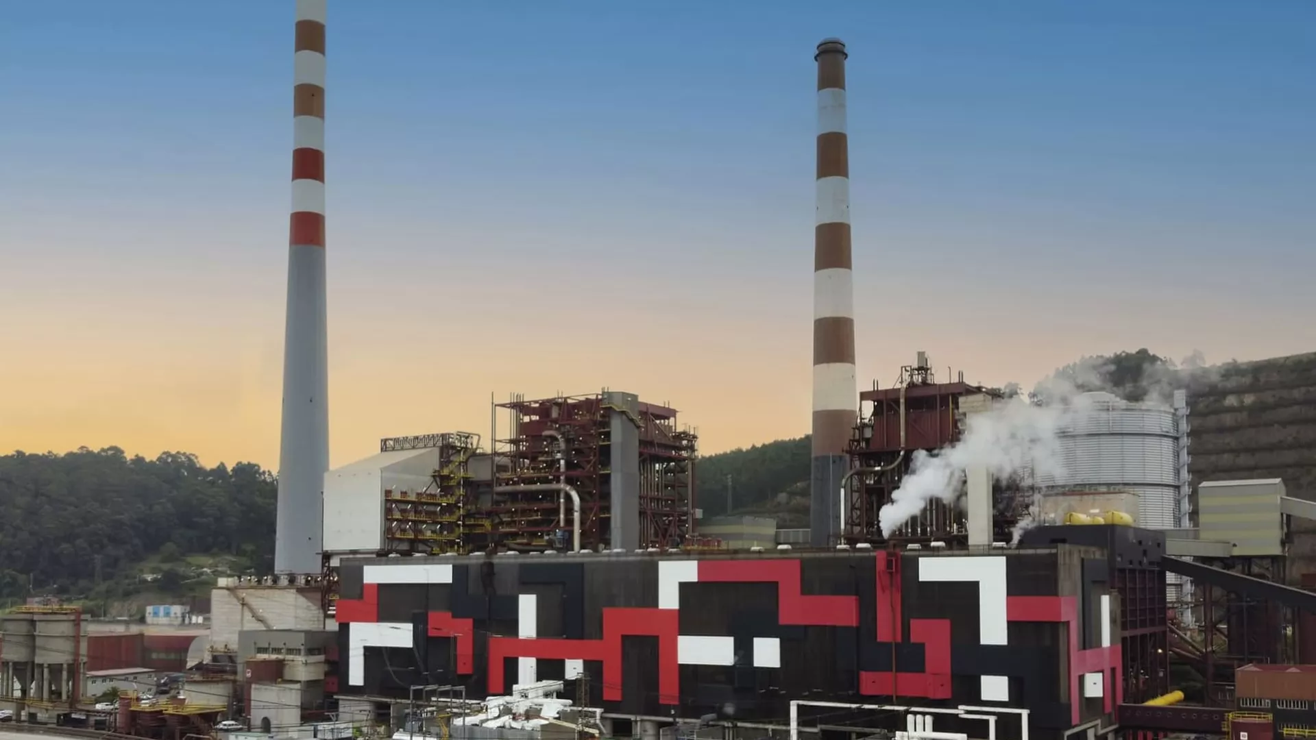 industrial site of a thermal power plant with two tall chimneys and geometric patterns on the exterior, surrounded by greenery and a clear sky